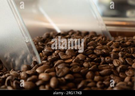 Pila di chicchi di caffè marrone tostati aromatici sparsi con cucchiaio di plastica Foto Stock