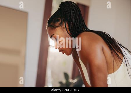 Donna che fa una pausa e prende fiato mentre si allena nella sua palestra di casa. Giovane donna che lavora sodo per ottenere il massimo dalla sua forma fisica e dal suo benessere Foto Stock