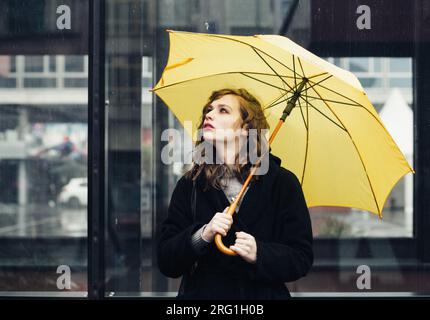 Giovane donna in città con un ombrello giallo Foto Stock