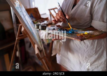 Primo piano delle mani di una donna che mescolano vernici a olio nel suo studio. Foto Stock