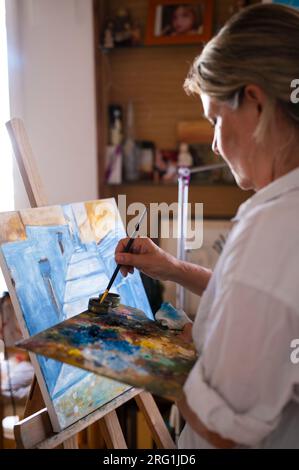 Donna matura che dipinge un dipinto ad olio nel suo studio. Foto Stock