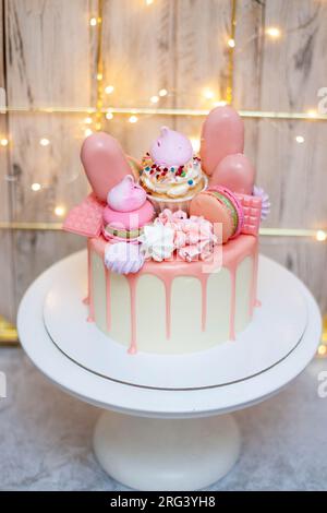 Bellissima torta decorata con cioccolato rosa fuso, macaron, meringhe, dolci e caramelle su sfondo festivo Foto Stock