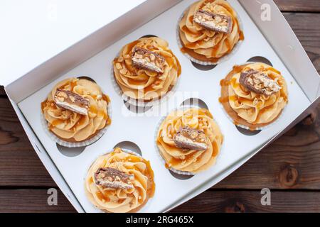 Stupendi cupcake con burro di arachidi, caramello salato e barretta di cioccolato sulla confezione regalo di cartone Foto Stock