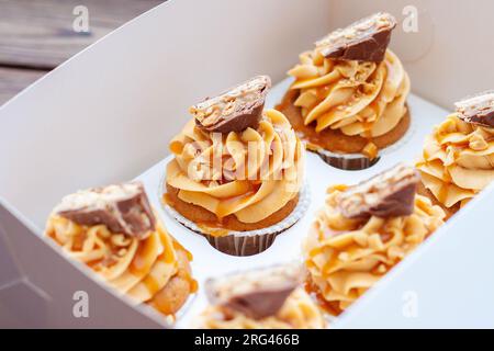 Stupendi cupcake con burro di arachidi, caramello salato e barretta di cioccolato sulla confezione regalo di cartone Foto Stock