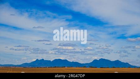 Panorama di montagne scure che si innalzano da una pianura agricola pianeggiante sotto un cielo blu con nuvole amichevoli. Stirling Range, Australia Occidentale Foto Stock