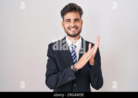 Giovane ispanico con tatuaggi che indossa abiti da lavoro e cravatta che applaude felici e gioiosi, sorridendo insieme mani orgogliose Foto Stock