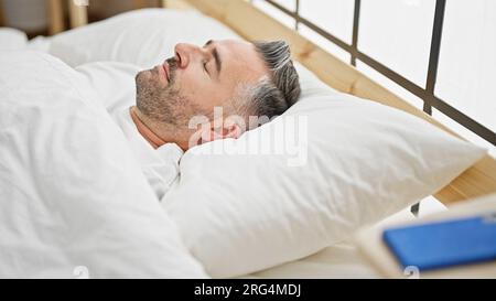 Uomo dai capelli grigi sdraiato sul letto che dorme in camera da letto Foto Stock