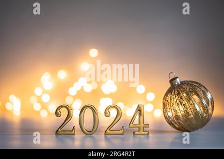 Numeri d'oro per il nuovo anno 2024 con una pallina di natale dorata su sfondo lucente e luci bokeh dall'atmosfera soffusa Foto Stock