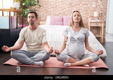 Coppia uomo e donna che si aspettano il ventre facendo esercizio di yoga in camera da letto Foto Stock