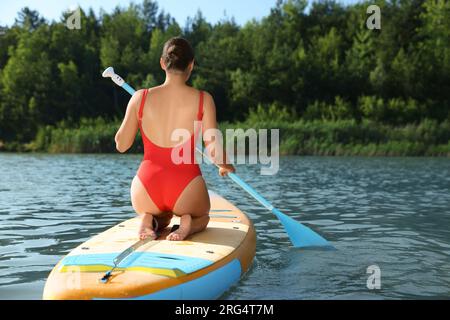 Donna che si imbarca su una tavola SUP nel fiume, vista sul retro Foto Stock