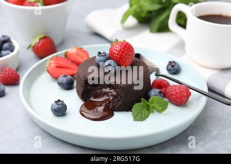 Piatto con delizioso fondente di cioccolato, frutti di bosco e menta su tavola grigia, primo piano Foto Stock