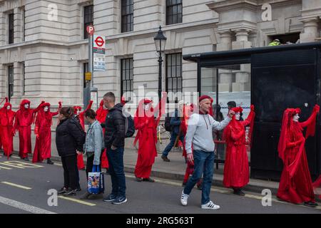 Londra, Regno Unito, 2023. Di fronte alla fermata dell'autobus di Whitehall, i turisti guardano la Brigata ribelle Rossa di Extinction Rebellion marciare verso Westminster Foto Stock