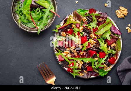 Insalata vegana con barbabietola, prugne secche, rucola, bietola svizzera e noci, fondo di pietra nera. Piatto vegetariano fresco e utile per un'alimentazione pulita Foto Stock