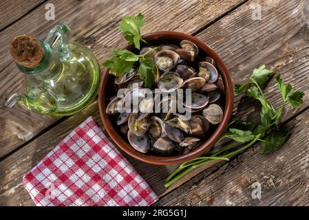 Casseruola di vongole grigliate su un tavolo di legno vintage con tovagliolo rosso a scacchi, ciuffi di prezzemolo e lattina d'olio. vista dall'alto Foto Stock