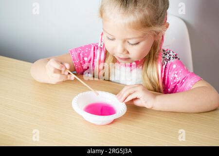 Carina ragazza caucasica sta facendo la melma da zero. Educazione dei bambini. A casa. Bambini che sperimentano. Foto Stock