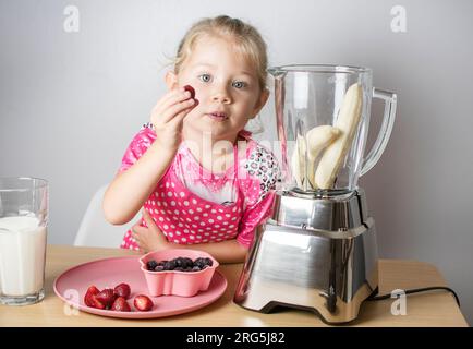 La graziosa ragazza caucasica sta cucinando un frullato. Bambini sani che mangiano. Imparare nuove competenze Foto Stock