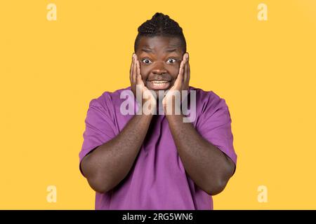 Emotivo afroamericano che guarda con stupore su sfondo giallo Foto Stock
