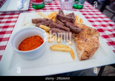 Cevapcici serviti con patate fritte, pane e salsa rossa, tipica cucina balcanica Foto Stock