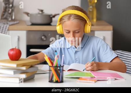 Bambino con le cuffie che fa i compiti in cucina Foto Stock