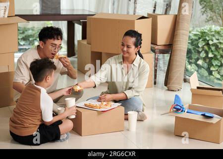 La madre dà al figlio una fetta di pizza quando mangia dopo aver imballato gli effetti personali Foto Stock