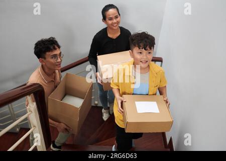 Famiglia felice che cammina al piano di sopra e porta con sé le valigie per un nuovo appartamento Foto Stock