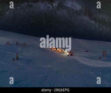 Gli amanti della neve (motoslitte) durante l'escursione notturna fanno un giro in cima alla montagna invernale con freerider snowboarder e cielo stellato con Milkyway abo Foto Stock