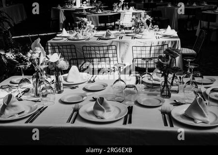 Tavoli splendidamente disposti con bicchieri, posate e stoviglie preparati per una grande festa. Fotografia in bianco e nero. Foto Stock