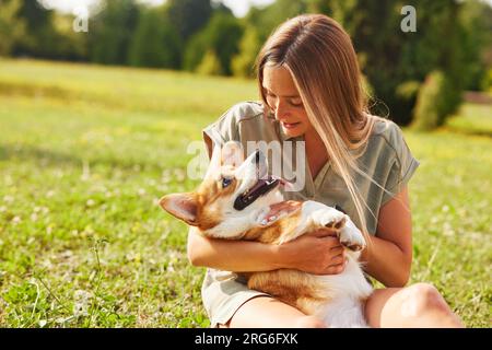 Una giovane ragazza tiene tra le braccia un allegro e divertente Corgi gallese in un parco con il sole, il concetto di cani felici Foto Stock