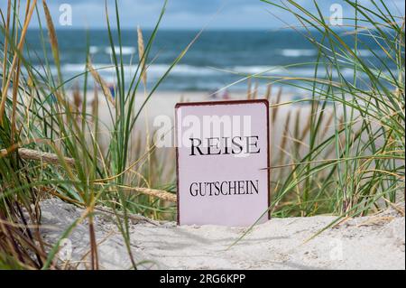 Il testo tedesco "Reise Gutschein" (voucher di viaggio) tra le dune di sabbia della spiaggia. Foto Stock