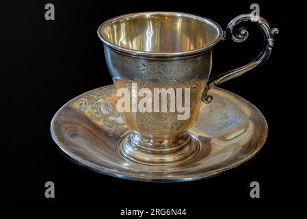 Tazza da tè e piattino antichi in argento sterling incisi su sfondo nero Foto Stock