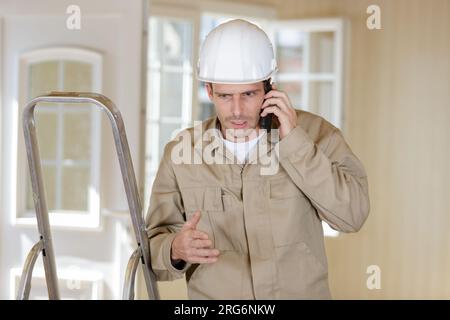 Builder sul telefono mediante una scala a pioli Foto Stock