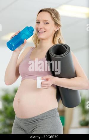 donna incinta che tiene un tappetino per esercizi e una bottiglia d'acqua Foto Stock