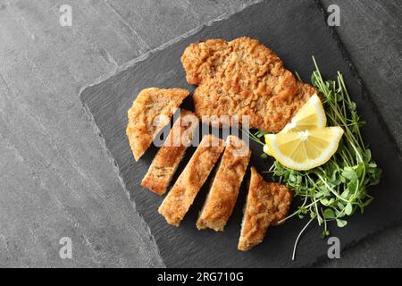 Gustosi schnitzels serviti con microgreen e limone su tavolo grigio, vista dall'alto Foto Stock