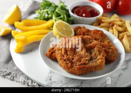 Gustosi schnitzels serviti con patatine fritte, ketchup e verdure su tavola di marmo, primo piano Foto Stock