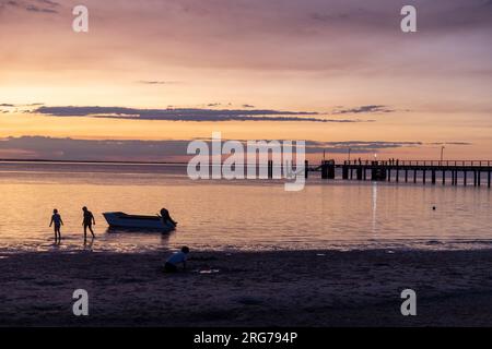 Fraser Island K'gari tramonto sulla Kingfisher Bay con sagome di barche e gente che costeggia le acque, Queensland, Australia Foto Stock