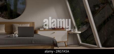 Un computer portatile su un letto in una camera moderna e confortevole in una notte di pioggia con gocce di pioggia su una grande finestra di vetro. Concetto di spazio di lavoro domestico. rendering 3d, 3d i. Foto Stock