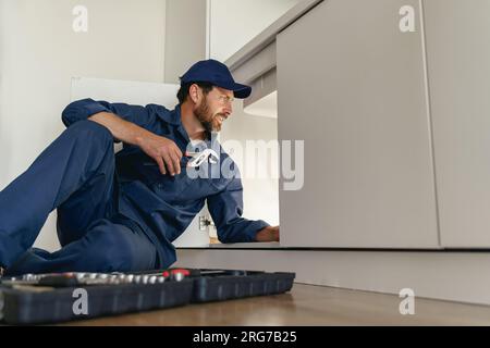 Idraulico professionale in uniforme blu fissaggio sifone rotto in cucina. Concetto di servizio di riparazione Foto Stock