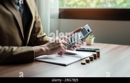 Uomo d'affari o contabile che utilizza la calcolatrice, calcola il report finanziario in ufficio, aiuta la pianificazione finanziaria e il risparmio per costruire ricchezza per il fut Foto Stock