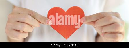 Donna in t-shirt bianca tiene il cuore rosso nelle mani davanti al corpo. Foto Stock