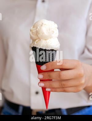 La mano di una donna tiene il gelato alla vaniglia in cono Foto Stock