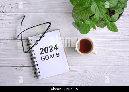 2024 goal su blocco note con tazza di caffè e occhiali da vista, vista dall'alto. Foto Stock