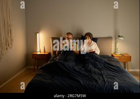 Coppia di famiglia tranquilla in pensione leggendo un libro insieme a letto Foto Stock