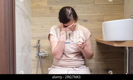 Una donna apprende della gravidanza seduta in bagno Foto Stock