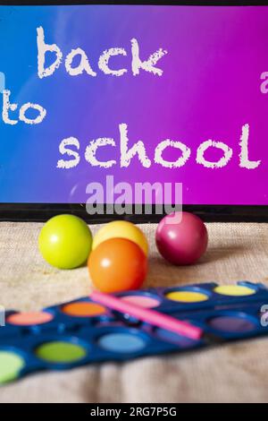 pastelli ad acquerello e palline colorate con l'iscrizione torna a scuola su una tavoletta Foto Stock