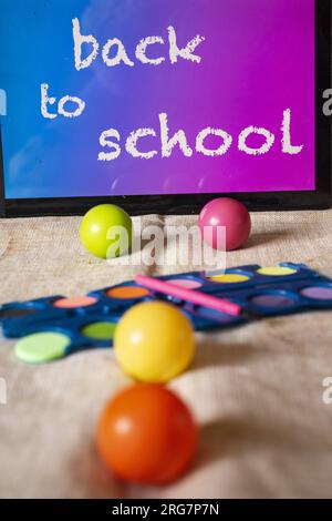 pastelli ad acquerello e palline colorate con l'iscrizione torna a scuola su una tavoletta Foto Stock