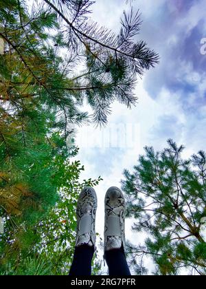 Piedi in scarpe autunnali, con stivali bianchi e neri contro il cielo e gli alberi. Gambe di donna in scarpe sullo sfondo di uno splendido paesaggio autunnale Foto Stock