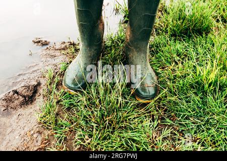 Agricoltore con stivali in gomma in piedi sul campo dopo una forte tempesta di pioggia in piantagioni allagate, concentrazione selettiva Foto Stock