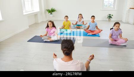 Gruppo di bambini che hanno una lezione di yoga, seduti su materassini, che fanno esercizi rilassanti e mediano Foto Stock