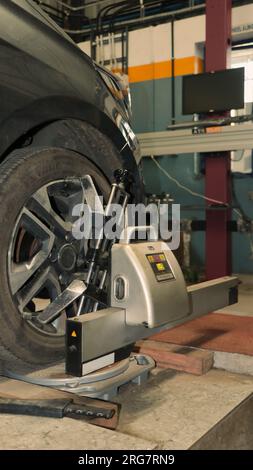 Uno pneumatico dell'auto sottoposto a manutenzione e correzione degli angoli di campanatura, incidenza e convergenza dello sterzo utilizzando un sensore di allineamento ruote 3D in un'officina di riparazione auto Foto Stock