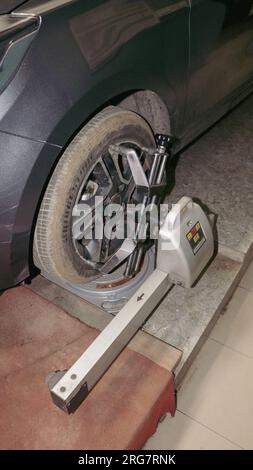 Uno pneumatico dell'auto sottoposto a manutenzione e correzione degli angoli di campanatura, incidenza e convergenza dello sterzo utilizzando un sensore di allineamento ruote 3D in un'officina di riparazione auto Foto Stock